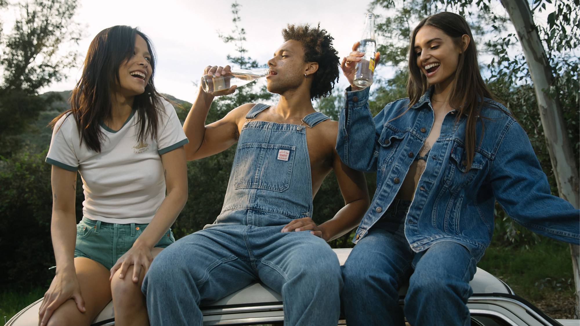 Models sitting on trunk of a car in assorted denim looks