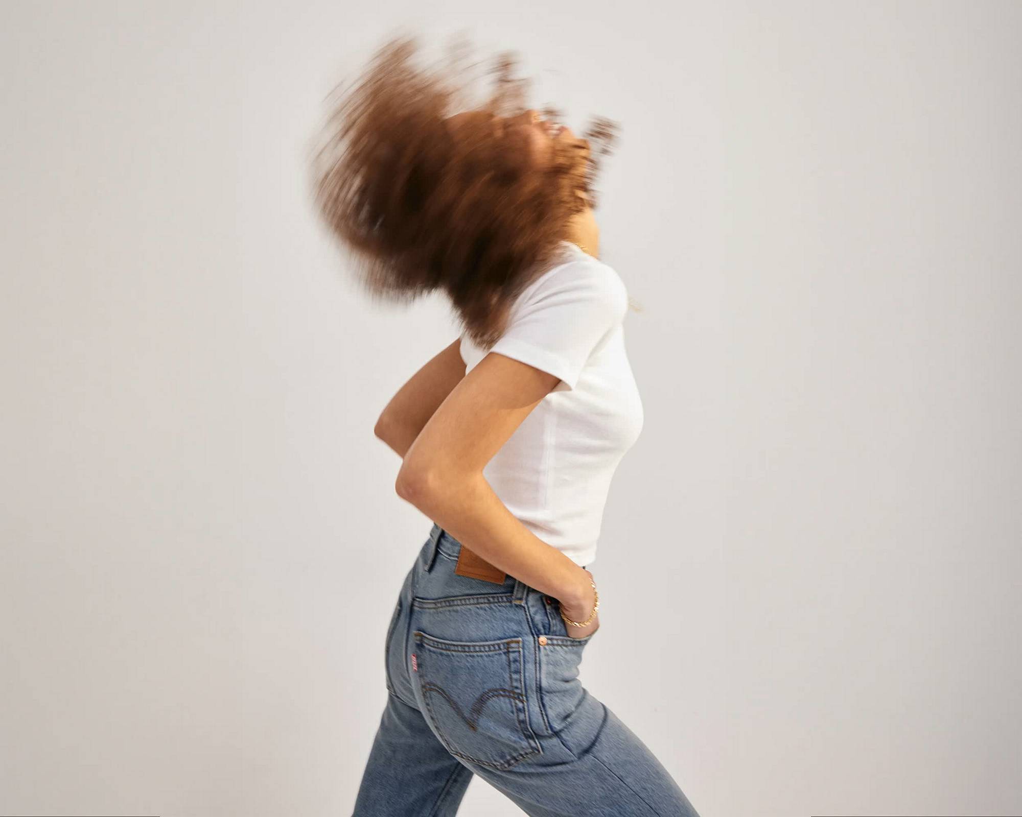 Split screen of model in motion wearing white tee and blue jeans with dark moody spotlight on stack of multi color button down shirts