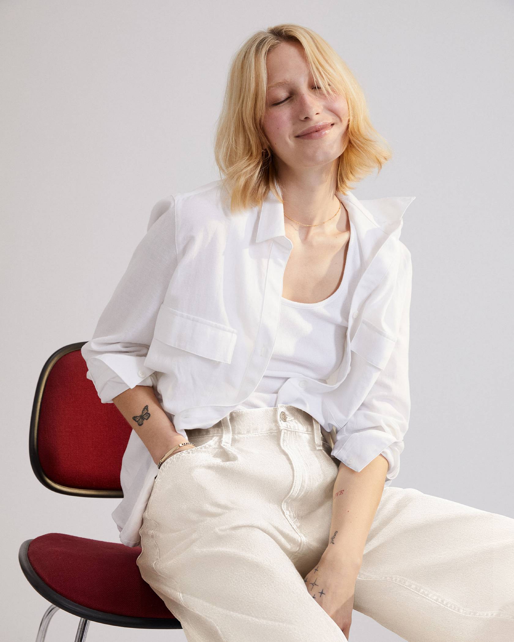 Model sitting on a chair in women's white button down top and cream colored baggy jeans