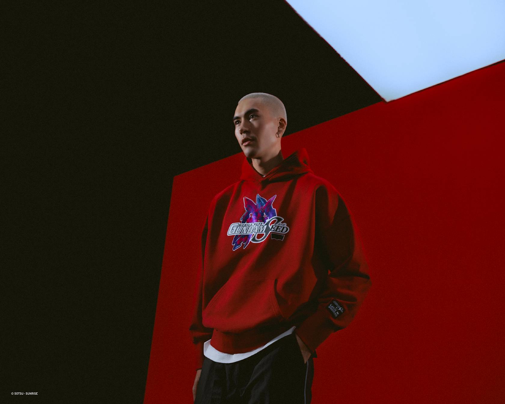 Image of male model wearing hooded red sweatshirt and posing against a futuristic background