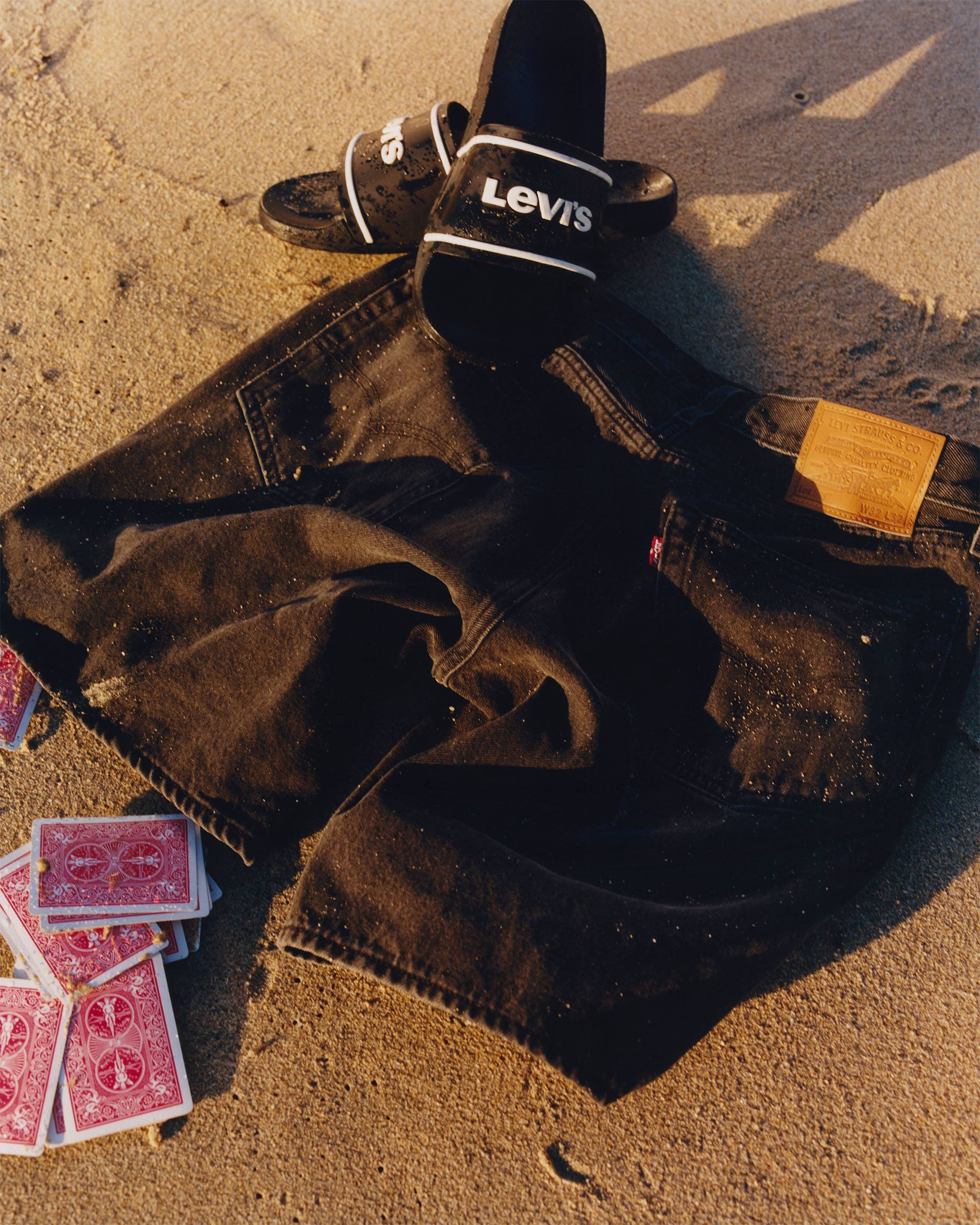 Men's black denim shorts laid out on a sandy beach