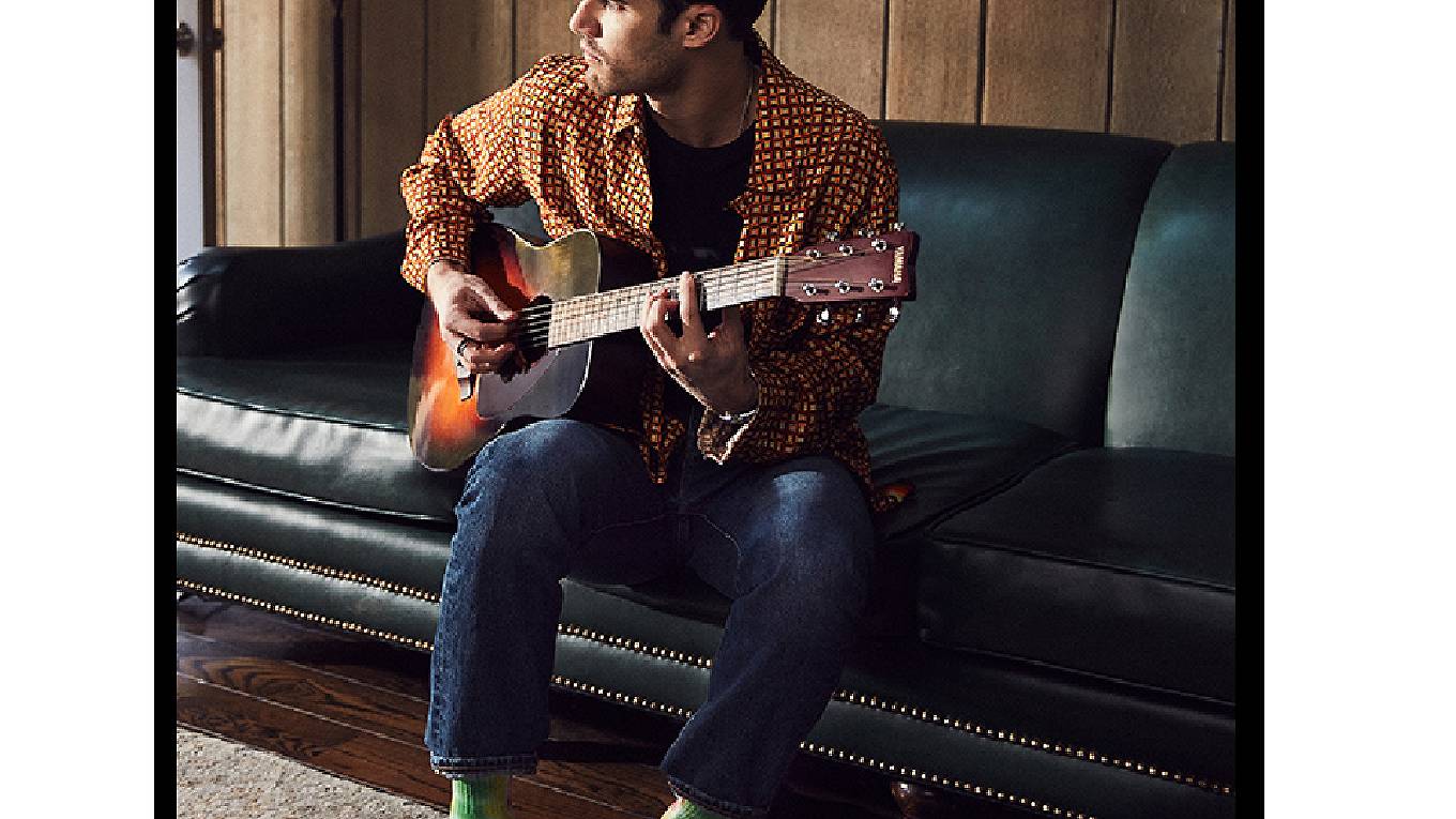 Criss sitting on the couch playing the guitar.