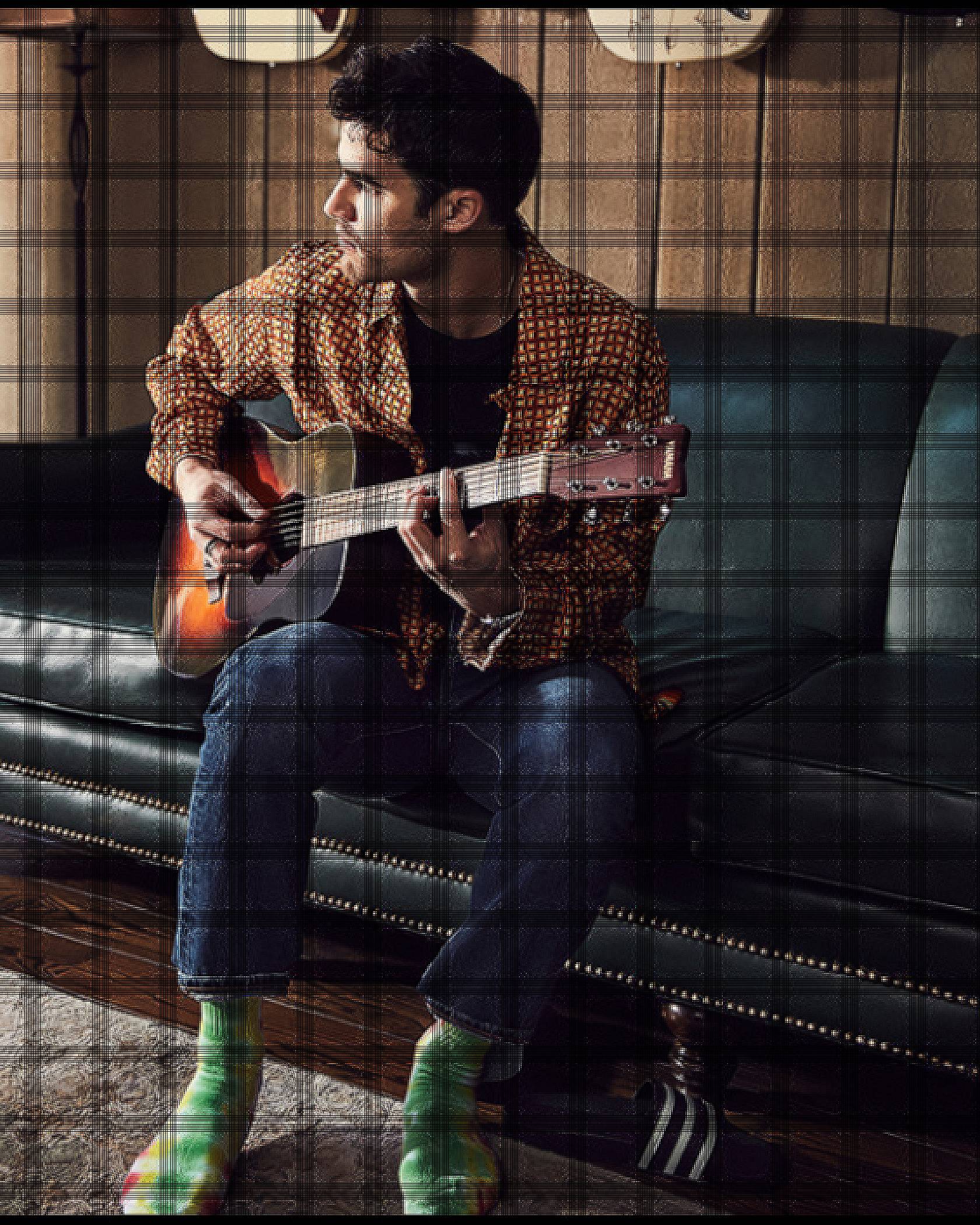 Criss sitting on the couch playing the guitar.