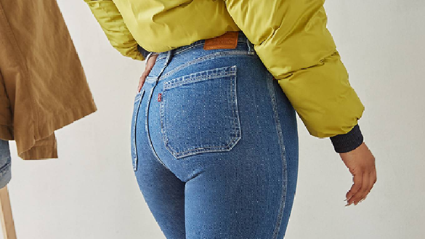 Image of Levi's® employee, Amber, wearing a pair of Levi's® Wedgie Jeans and a mustard yellow jacket with her left hand in her left back pocket.