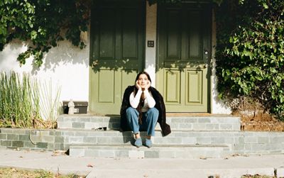 Portrait of ABIR sitting on a stoop with her head resting in both palms.