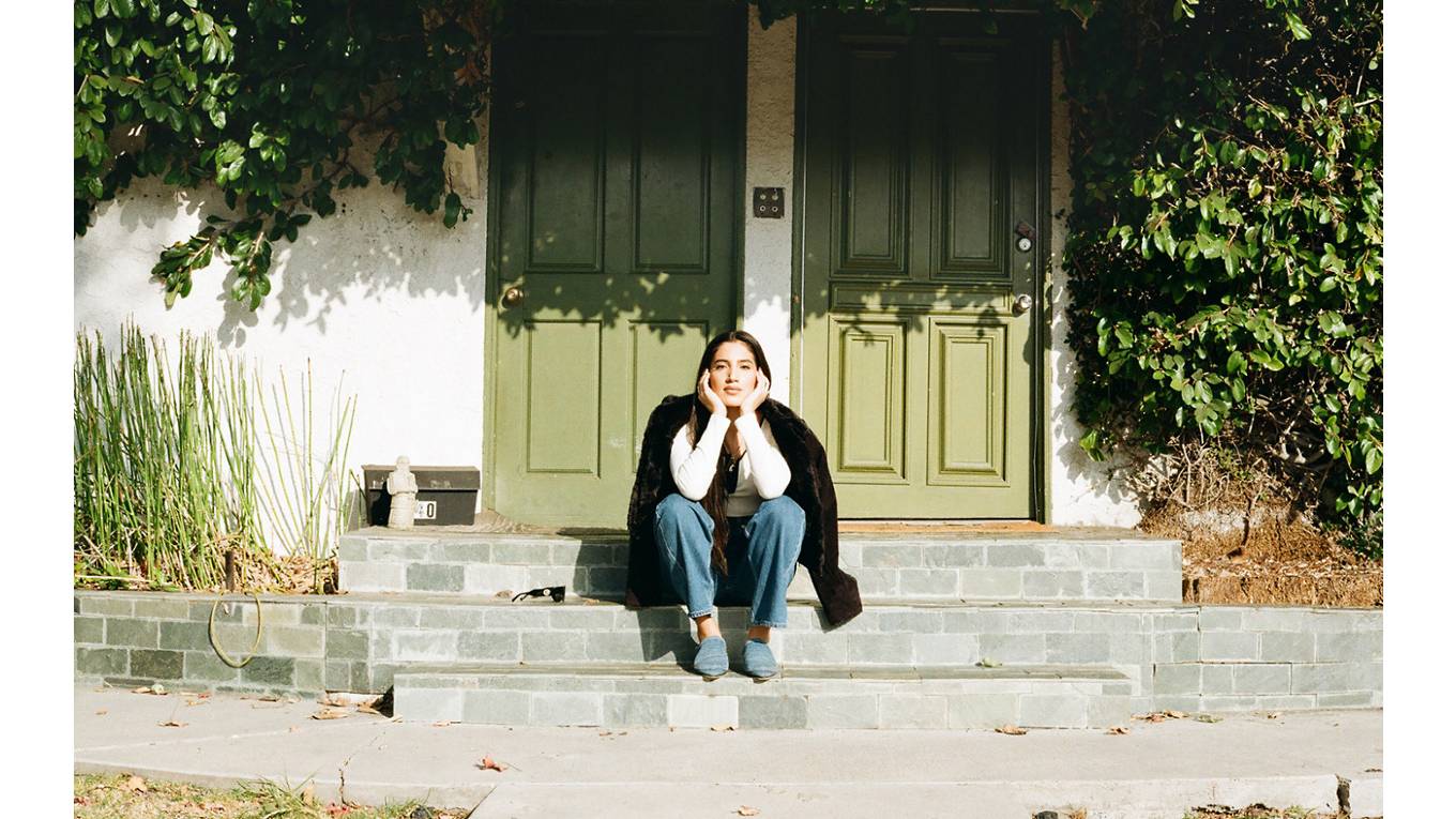 Portrait of ABIR sitting on a stoop with her head resting in both palms.