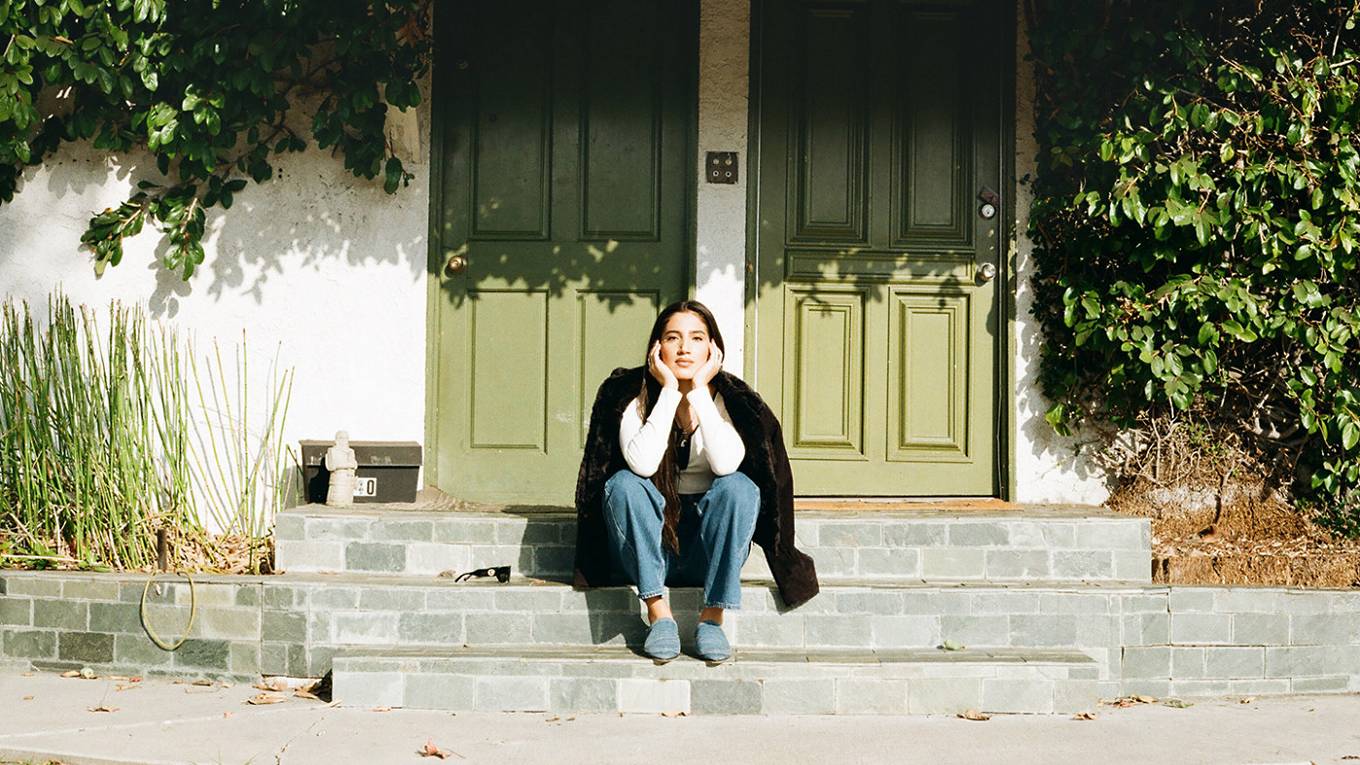Portrait of ABIR sitting on a stoop with her head resting in both palms.
