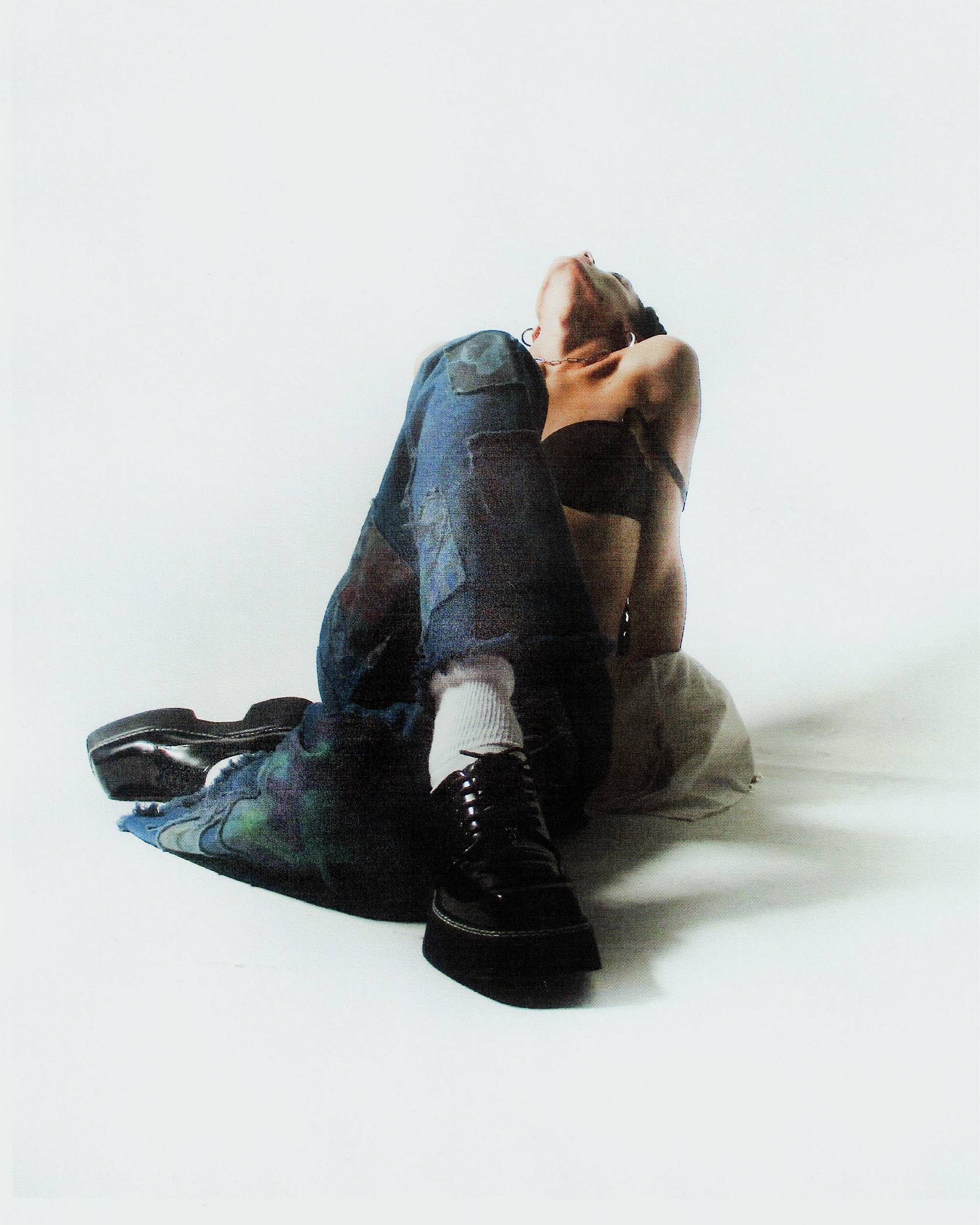 Model sitting on the floor with legs crossed in the blue colored collab jeans and black bra