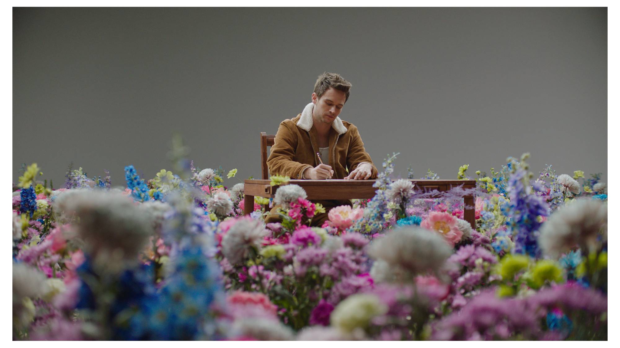 Brandon Flynn sitting at a desk in a field of flowers