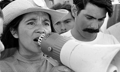 A black and white photo of a woman speaking into a megaphone with a hat on.