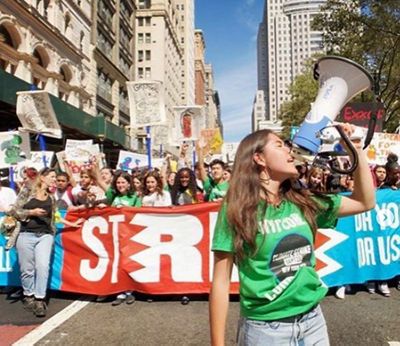 A photo of Xiye with a loud speaker standing in front of a rally on a city street.