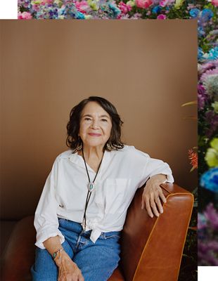 A portrait shot of Dolores sitting down in a leather brown chair, wearing a white shirt, smiling at the camera