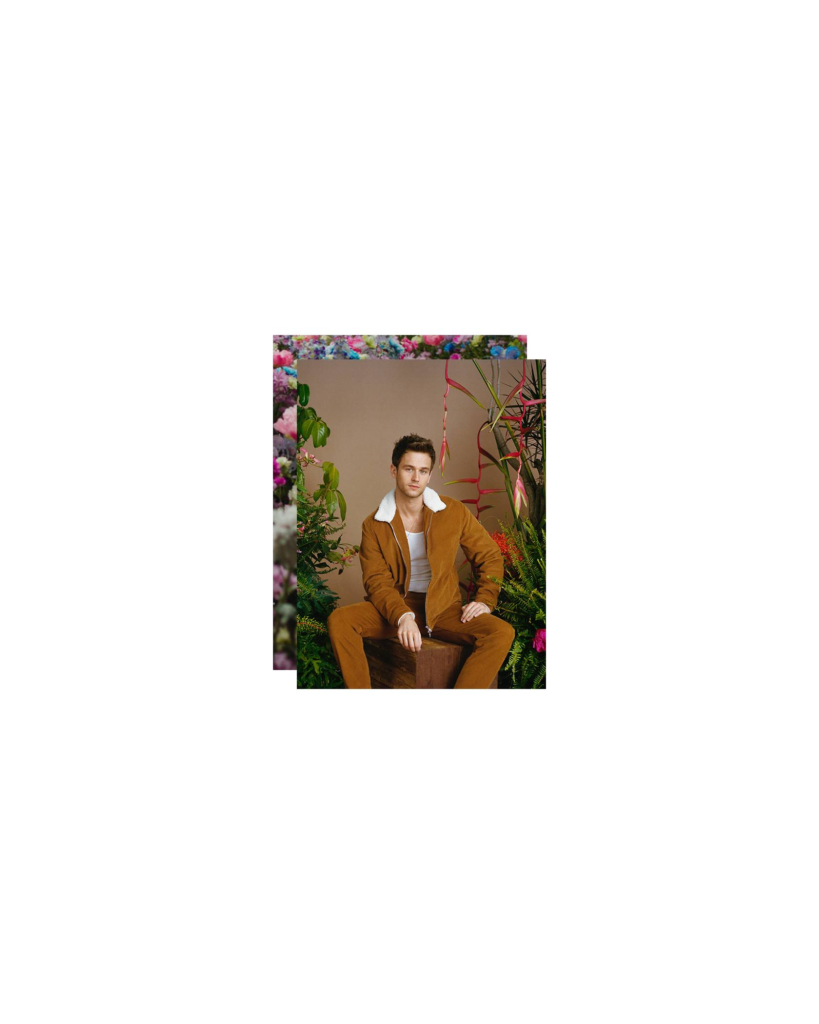 Brandon Flynn sitting on a wooden stool, surrounded by plants.