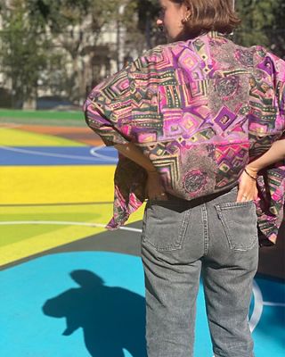Photo of Sarah Coburn standing on a basketball court. Her back is to the camera and she's wearing a bright printed shirt and black Levi's jeans.
