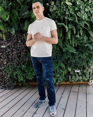 Callen Schaub standing in front of a wall of plants, rocking his pair of Levi's® Future Finish dark wash jeans and an off-white colored Levi's® tee shirt with his hands in front of him.