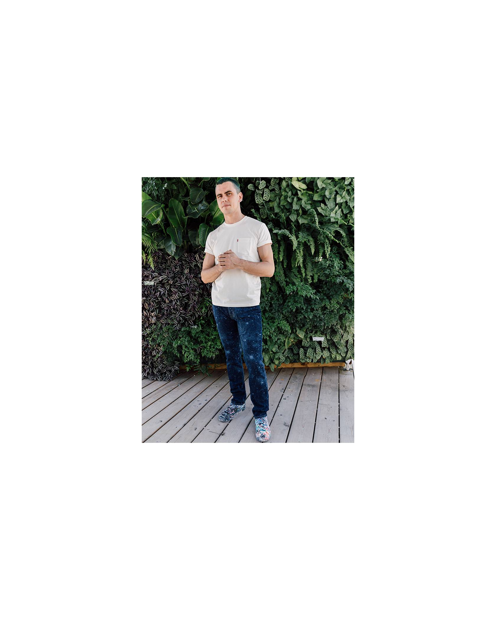 Callen Schaub standing in front of a wall of plants, rocking his pair of Levi's® Future Finish dark wash jeans and an off-white colored Levi's® tee shirt with his hands in front of him.