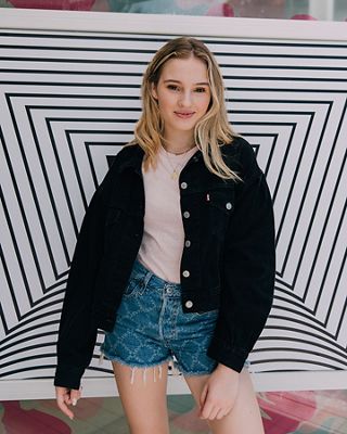 TikToker Cosette stands in front of a black and white background, wearing a black denim trucker jacket, pink tee shirt, and Levi's® Future Finish 501® shorts.