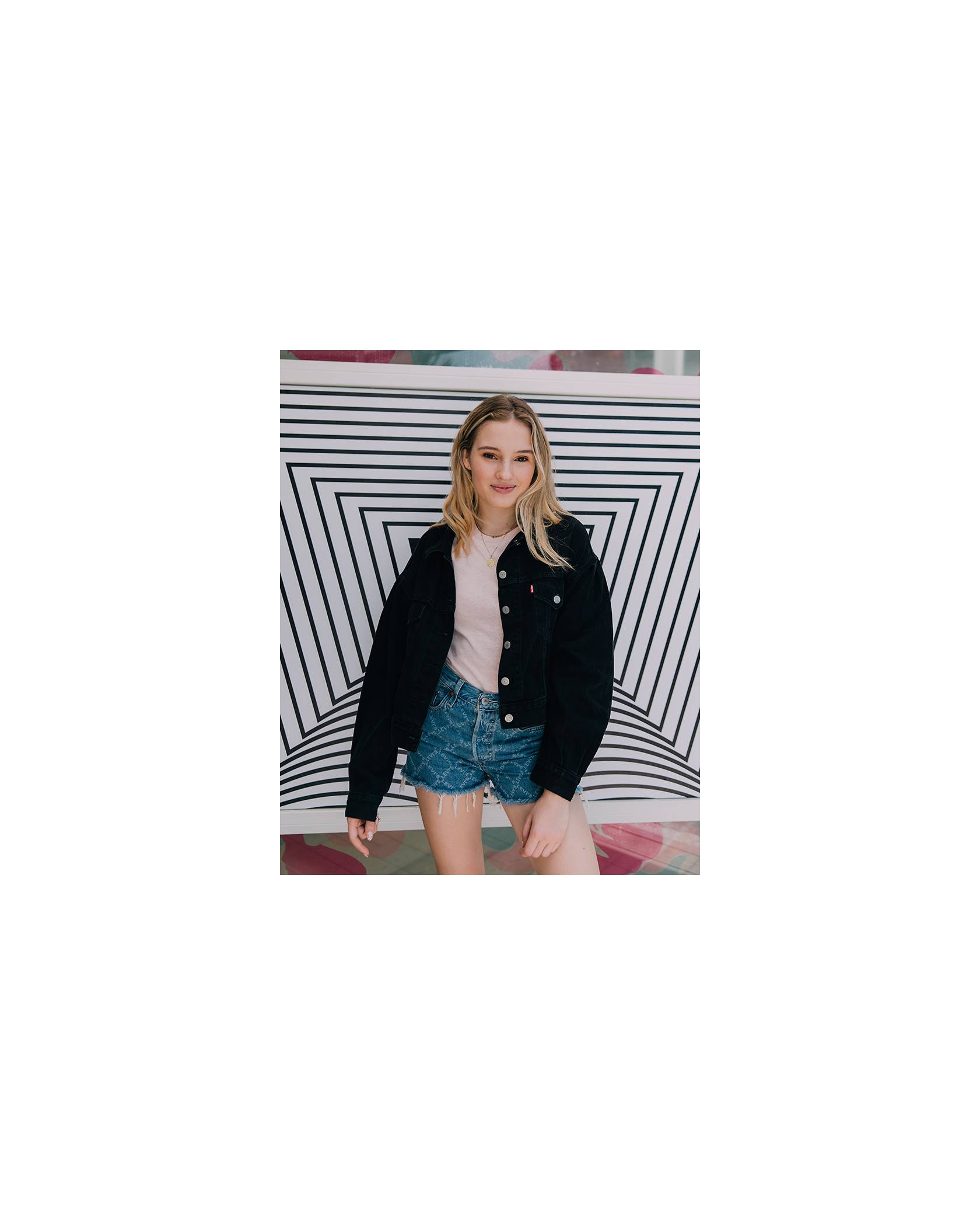 TikToker Cosette stands in front of a black and white background, wearing a black denim trucker jacket, pink tee shirt, and Levi's® Future Finish 501® shorts.