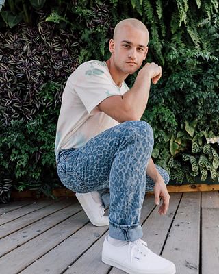 TikToker Everett Williams kneels on the ground in front of a wall of plants while wearing his cheetah print light wash Levi's® Future Finish jeans.