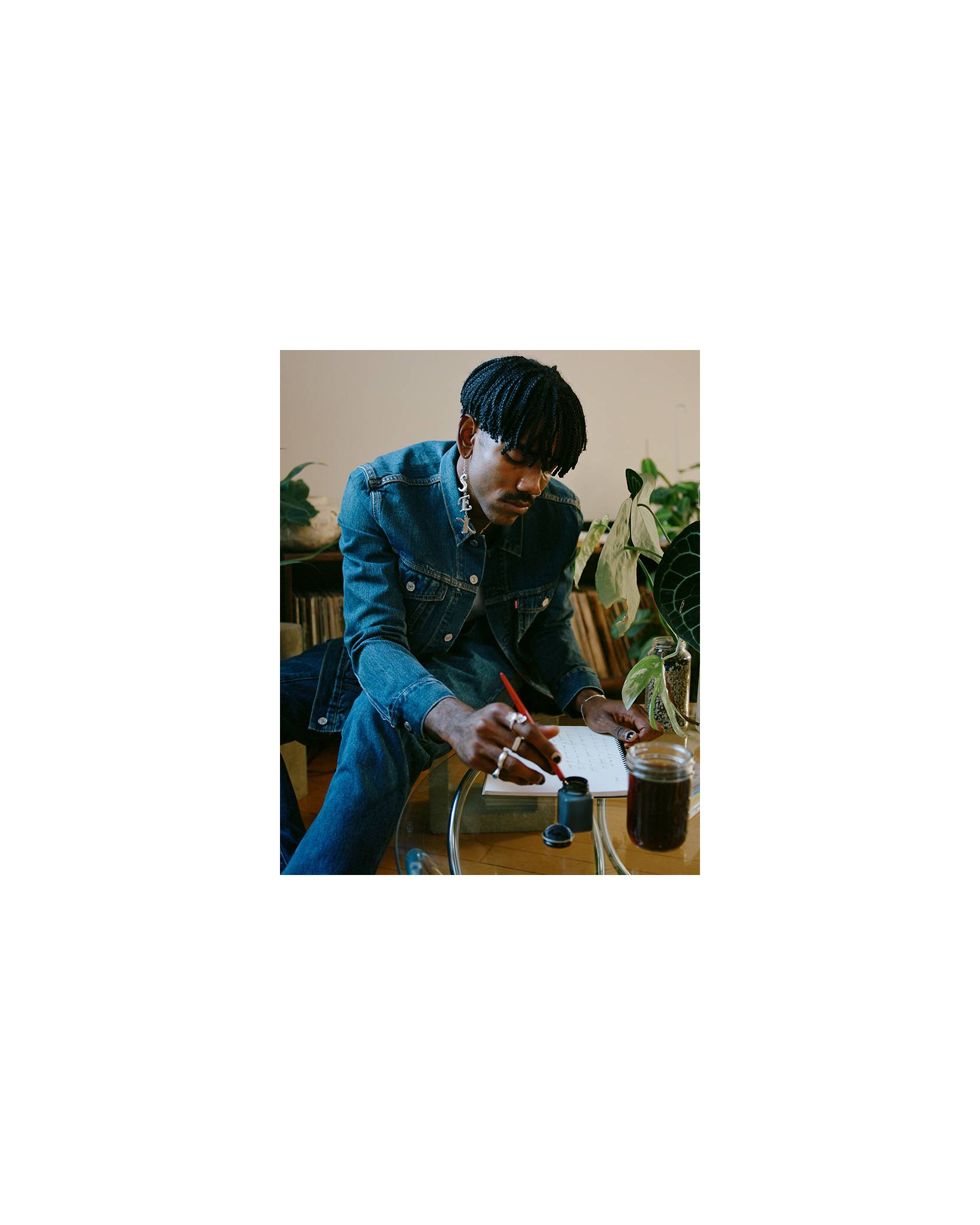 Photo of Jerrod La Rue in a Levi's Trucker Jacket and jeans writing in his notebook with a glass of iced coffee on the table.
