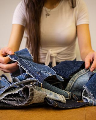 Bria Cheng repairing a pair of jeans wearing a white shirt.