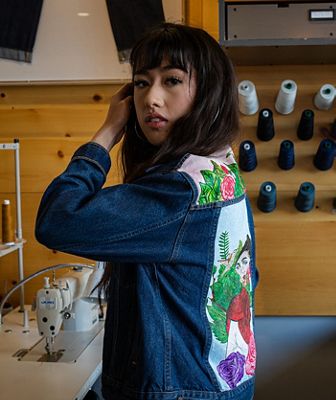 Bria Cheng wearing a custom denim jacket and holding her hair behind her ear.