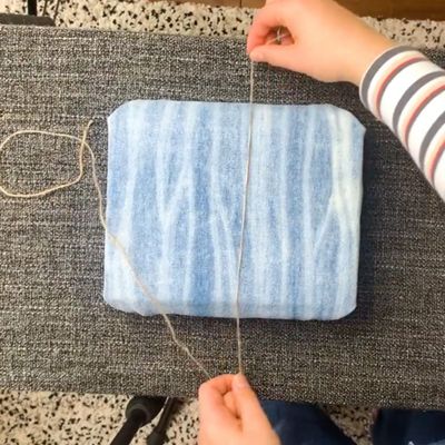 hands tying twine around denim gift box