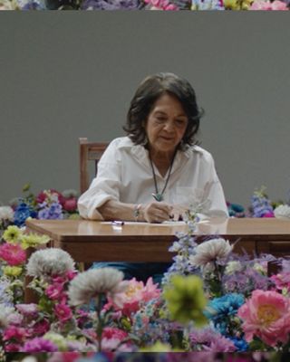 Split screen images of Dolores Huerta and Xiye Bastida both separately writing on a wooden desk, surrounded by flowers.