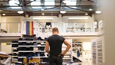 Image of Bart Sights standing in the middle of the Eureka Lab, looking down at denim jeans with a Pride flag hanging on the left.
