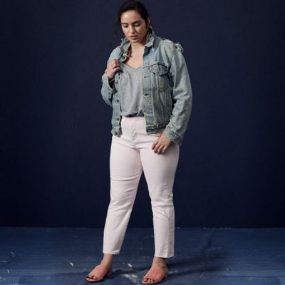 Light denim jacket with white denim jeans, woman standing in front of a dark blue background.