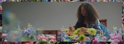 Naomi Osaka writing on a wooden table, surrounded by flowers.