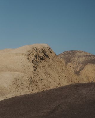 Image of a large mountainside against a bright blue sky.