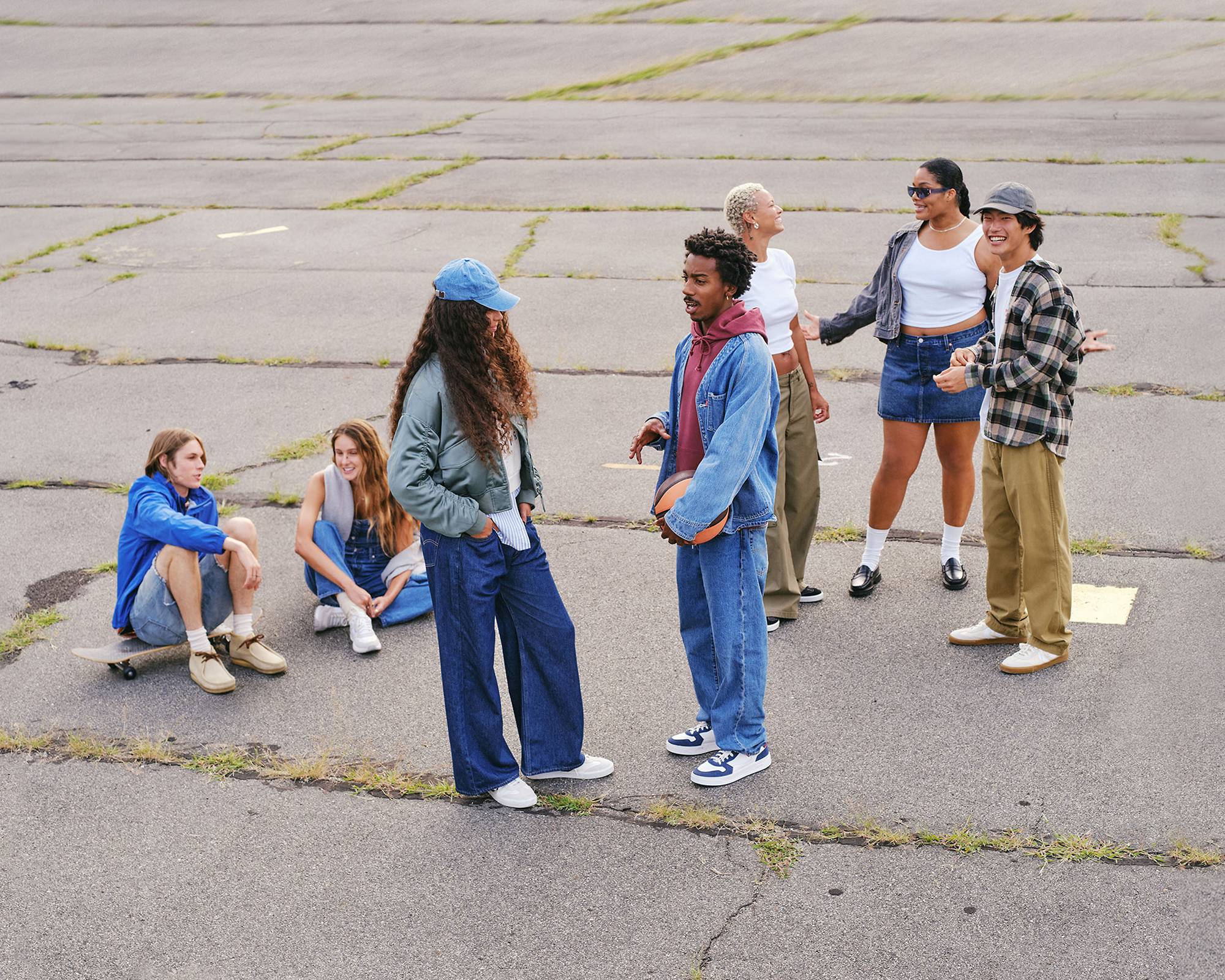 Large group shot of models outdoors in concrete lot wearing assorted denim looks and casual streetwear
