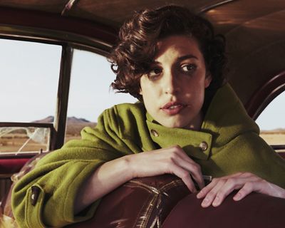 Woman in a green jacket looking over the back seat in a car.