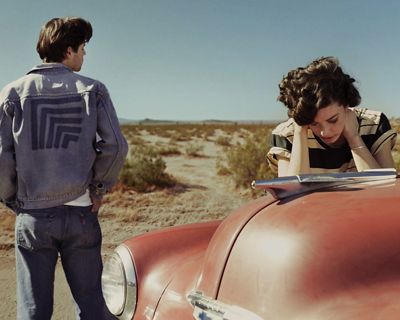 Man and woman stranded in the desert and the woman leaning on the car.