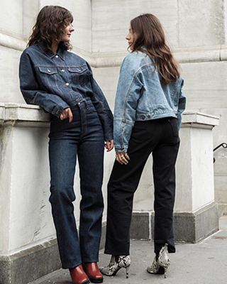 Bffs matching and wearing light and dark denim jackets lounging on a wall.