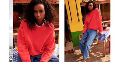 Woman wearing an orangeish sweater and lounging against a table.