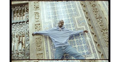 Man standing in front of mosaic background with his arms spread open.