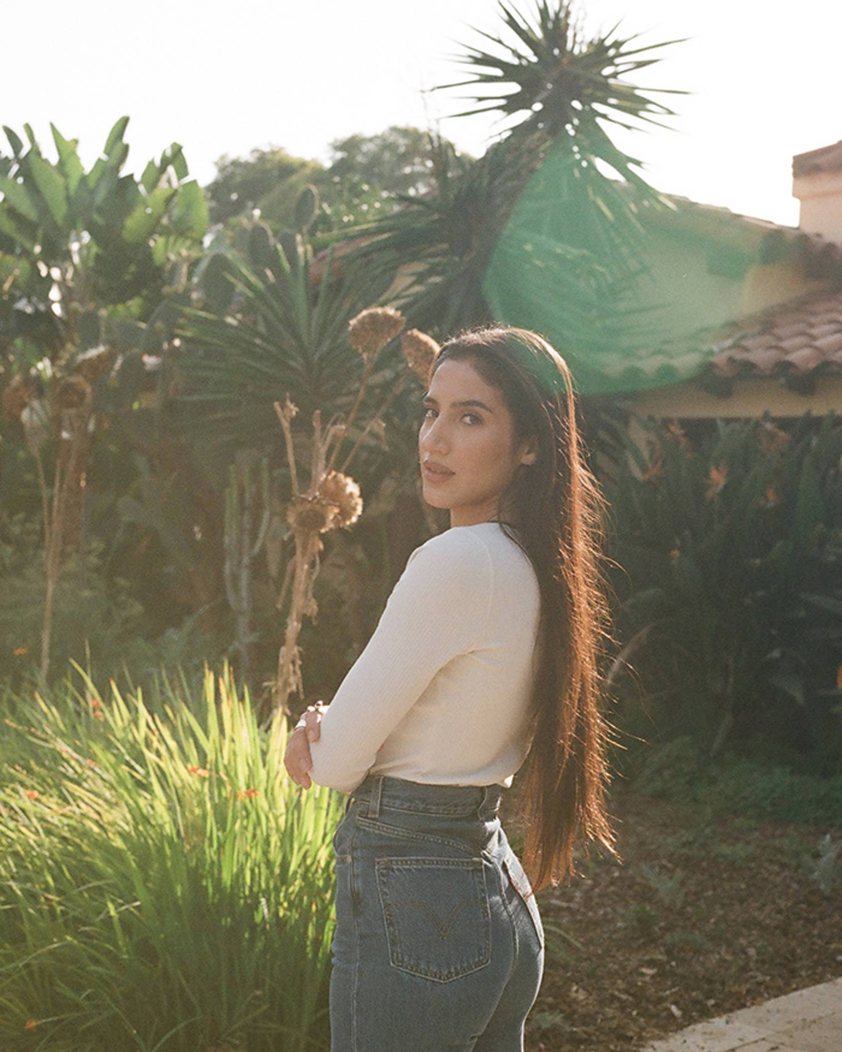 Portrait of ABIR standing outside in a white long-sleeve shirt and Levi's jeans.