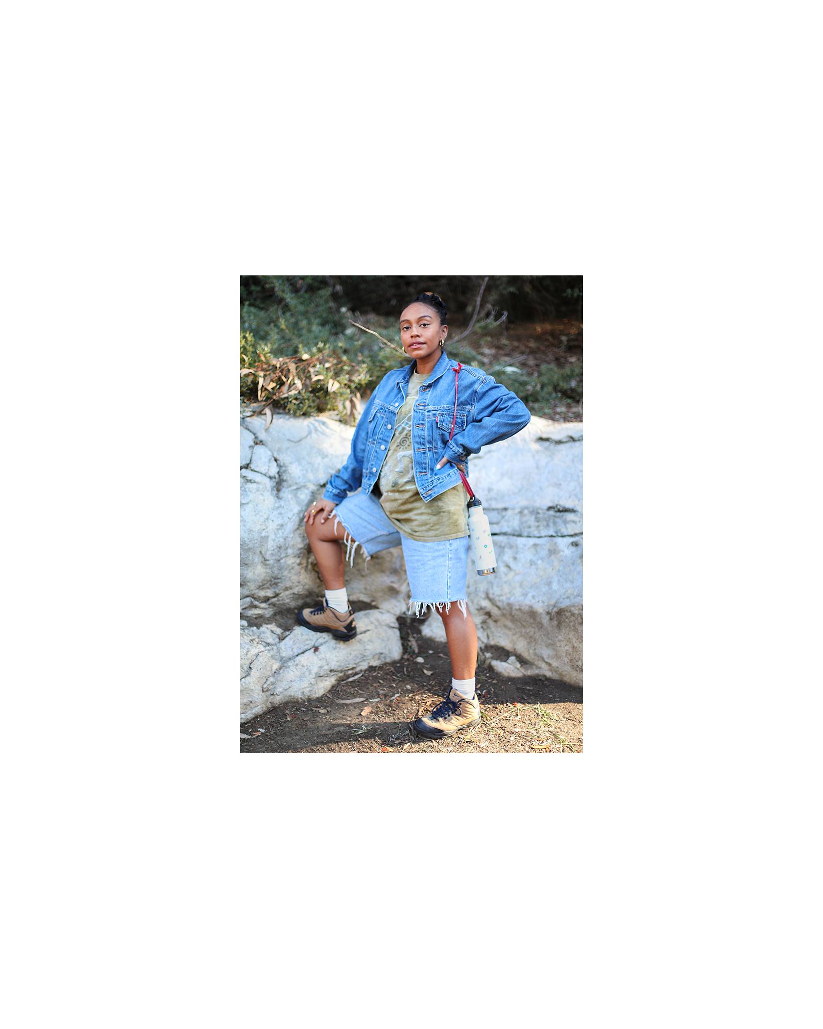 Photo of Evelynn Escobar-Thomas outdoors, wearing a Levi's Trucker Jacket, a tie-dye shirt, and denim cut-offs with hiking shoes.