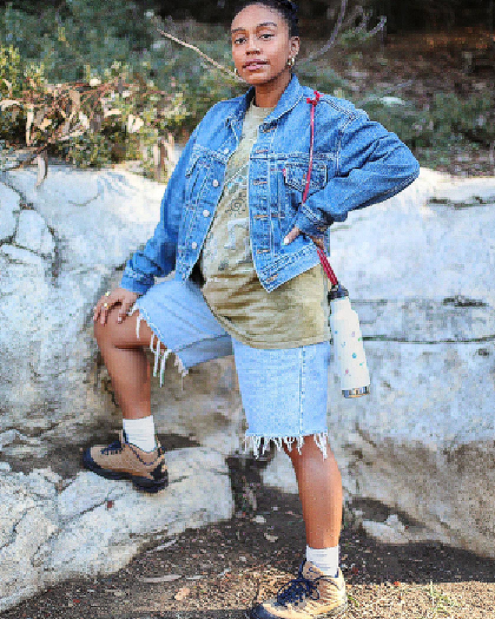 Photo of Evelynn Escobar-Thomas outdoors, wearing a Levi's Trucker Jacket, a tie-dye shirt, and denim cut-offs with hiking shoes.