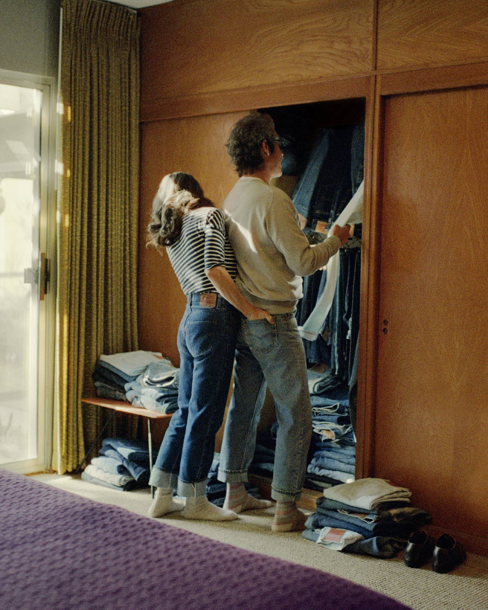 A husband and wife standing in their bedroom looking in their closet, both wearing Levi's jeans.
