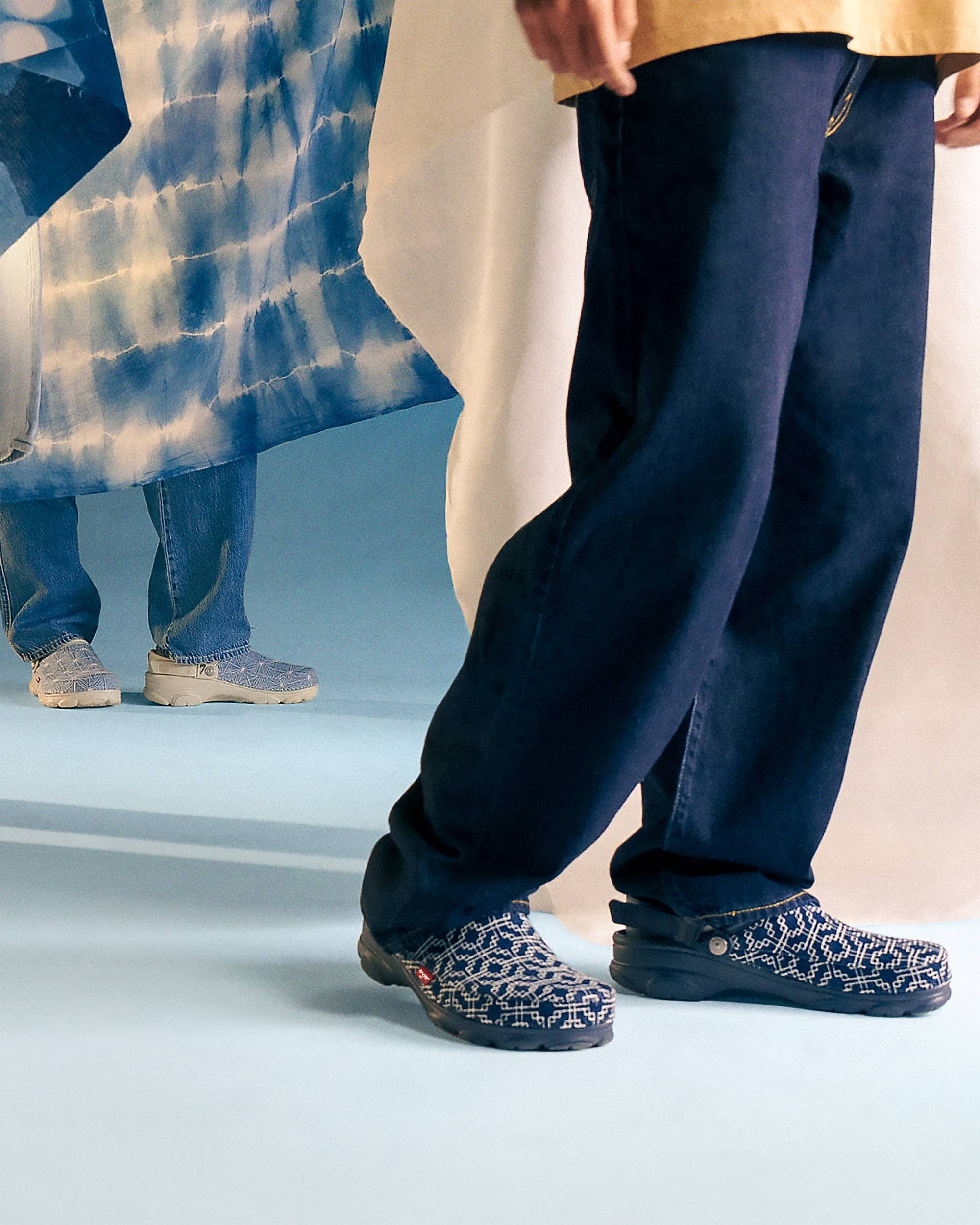 Levi's x Crocs shoes made out of denim on a person with jeans on with a blue background.