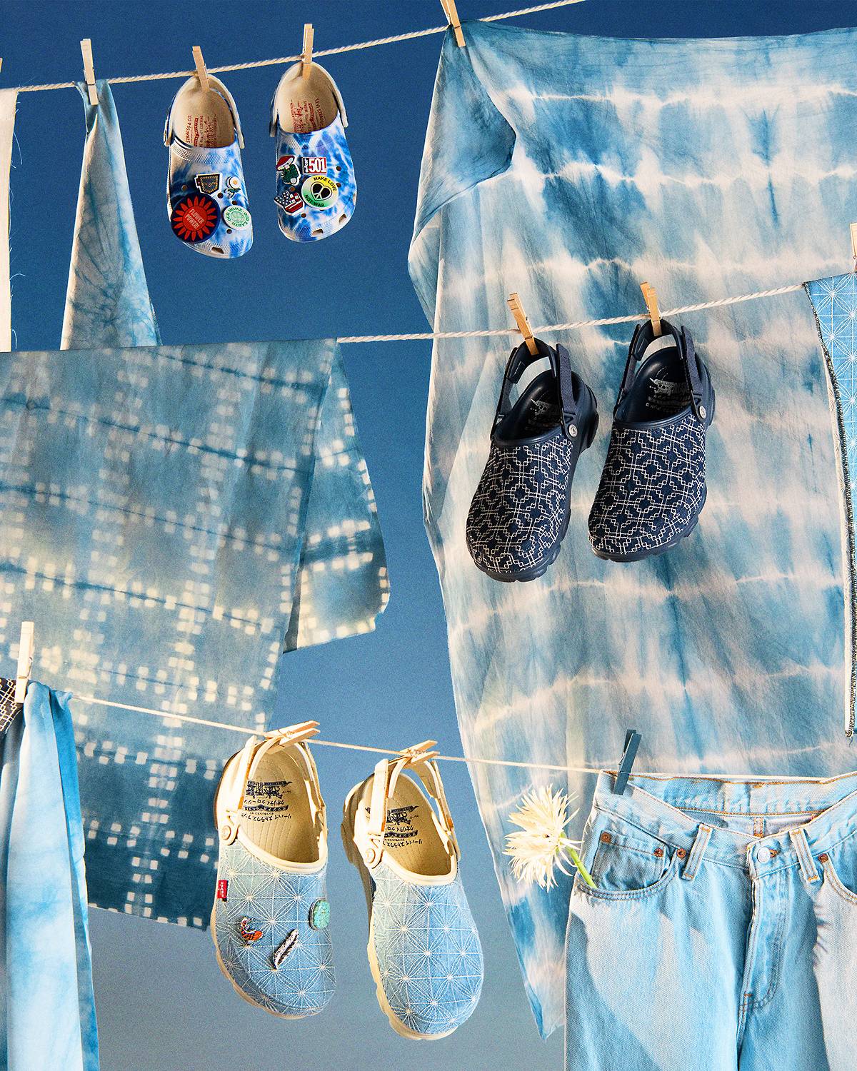 Three pairs of the Levi's® x Crocs collaboration hanging on a clothesline with pieces of dyed fabric hanging in the background.