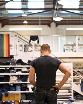 Image of Bart Sights standing in the middle of the Eureka Lab, looking down at denim jeans with a Pride flag hanging on the left.
