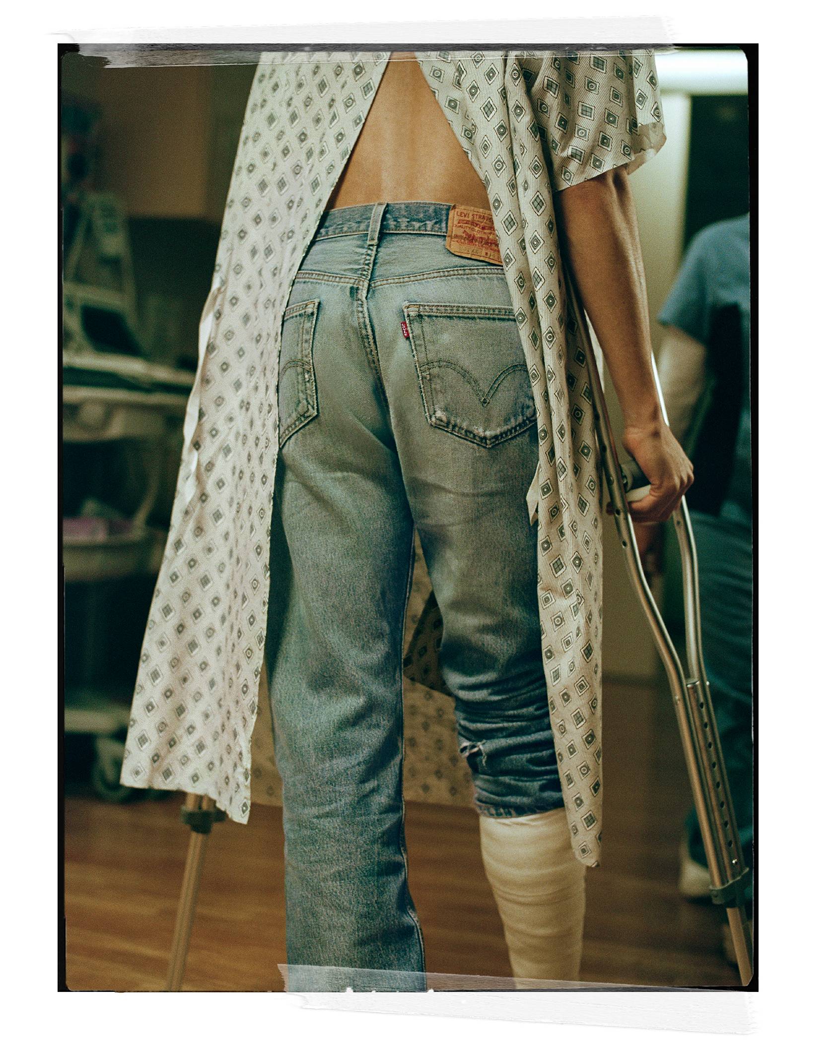Person wearing Levi's jeans with a hospital gown on, cast on a foot while walking with crutches.