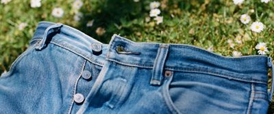 Lay-down image of a pair of blue jeans against grass with daisies surrounding it.
