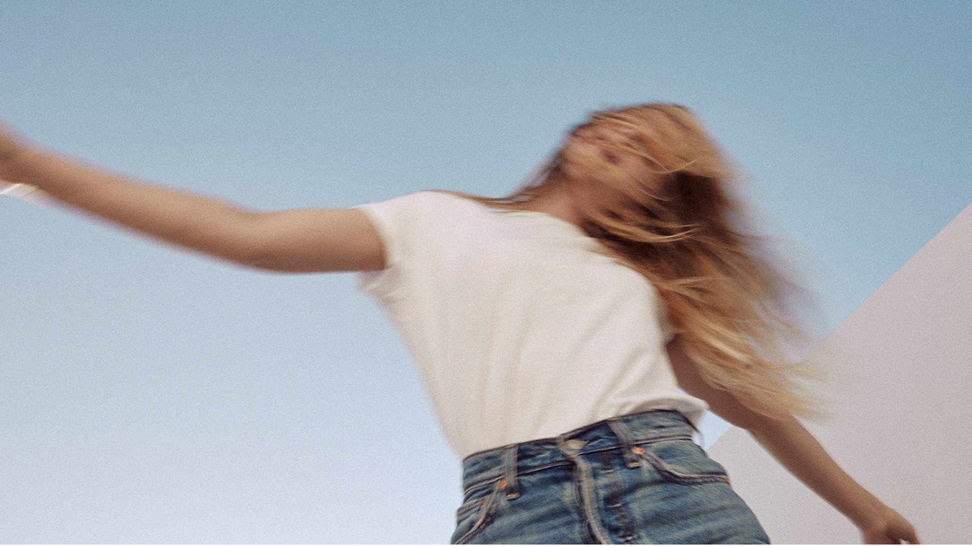 Blurry image of a woman wearing a white tee and Levi's jeans set against a blue sky.