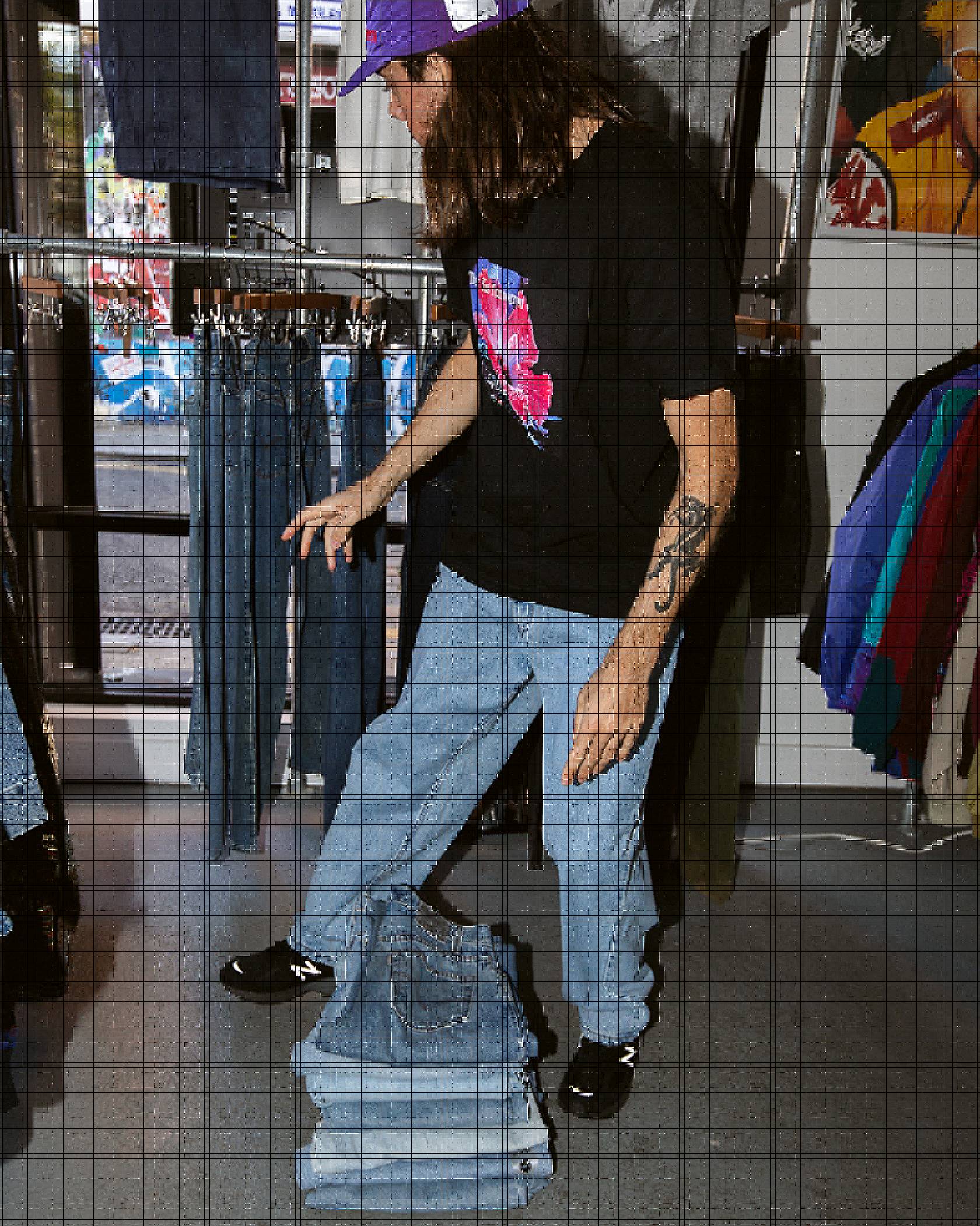 Photo of Sam Trotman inside a vintage clothing store, looking at a rack of blue jeans. There is another stack of folded jeans on the floor in front of him.