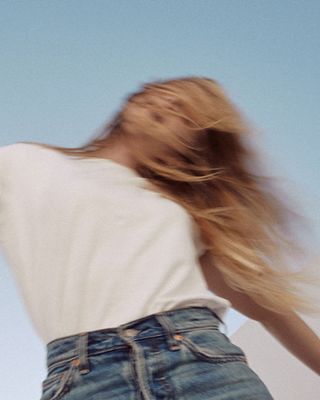 Blurry image of a woman wearing a white tee and Levi's jeans set against a blue sky.